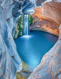 Waterfall flowing into blue pool within colorful layered slot canyon walls
