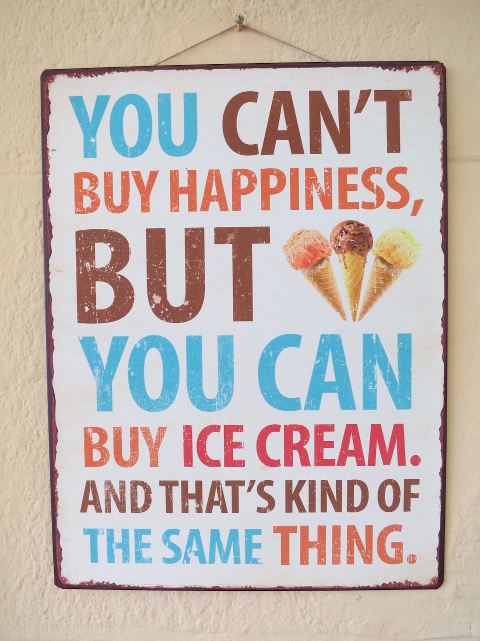 Metal wall sign reading 'You can't buy happiness but you can buy ice cream' with three ice cream cone illustrations
