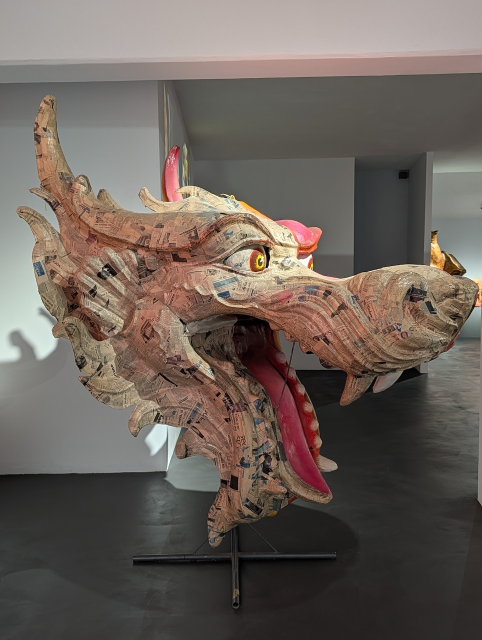 Papier-mâché dragon head sculpture with open mouth on display stand in museum gallery