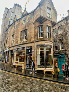 Stone corner building with The Milkman cafe on a coblestone Edinburgh street with bunting flags