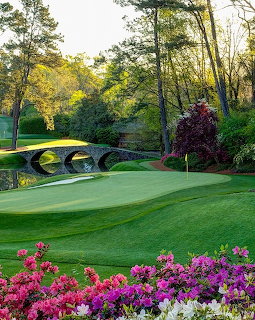 Augusta National golf course with stone bridge, green fairway, azaleas, and pine trees