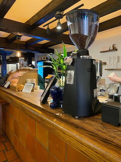 Black commercial espresso grinder on wooden coffee shop counter with cafe interior in background