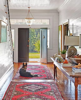 Foyer with white walls, dark door, Persian rug runner, console table, chandelier, and black dog sitting on rug