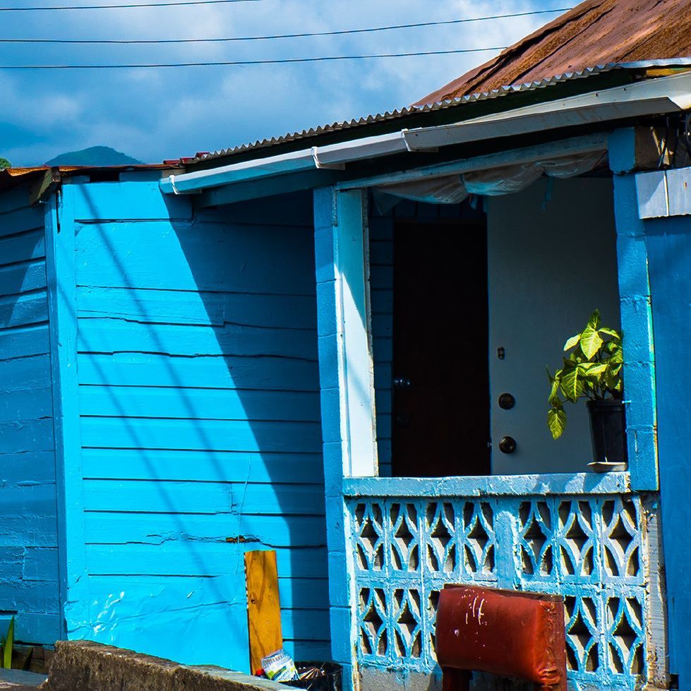 Bright blue wooden house with a porch, lattice railing, and rusted roof