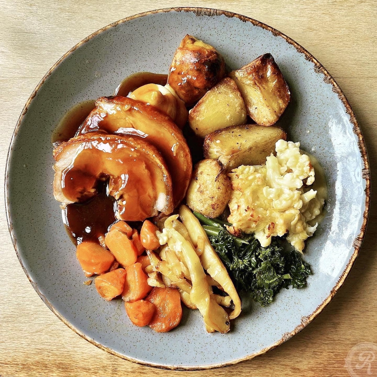 Overhead view of a dinner plate with roasted meat, vegetables, and greens on a wooden surface