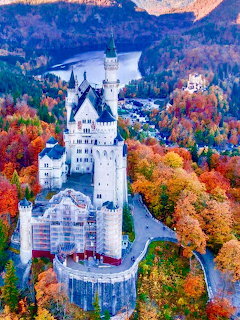 White fairy-tale castle with towers amid colorful fall foliage and mountains