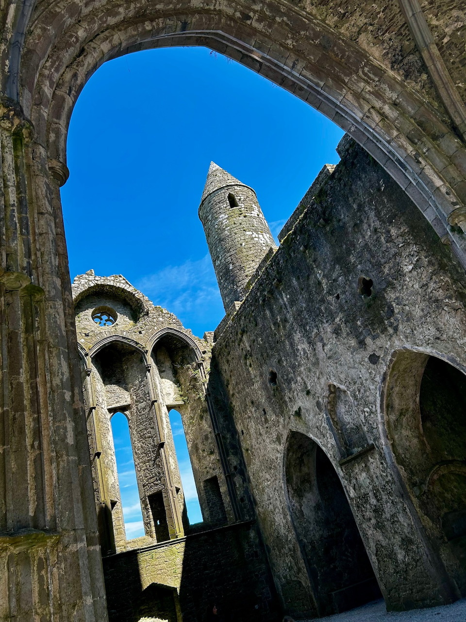 Stone castle ruins with arches and a round tower seen from below against a blue sky