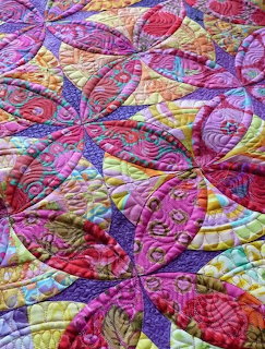 Colorful patchwork quilt with circular pinwheel patterns in pink, purple, yellow, and orange fabrics