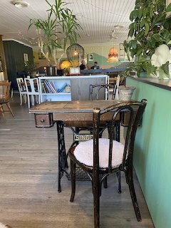 Restaurant interior with wooden tables, black chairs, and hanging plants in a bright dining room