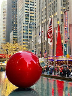 Giant red Christmas ornament ball at Rockefeller Center, New York City, with skyscrapers and flags in background