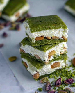 Stack of three green matcha layered dessert bars with white cream and pistachios