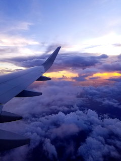 Airplane wing viewed from window against sunset clouds and purple-orange sky
