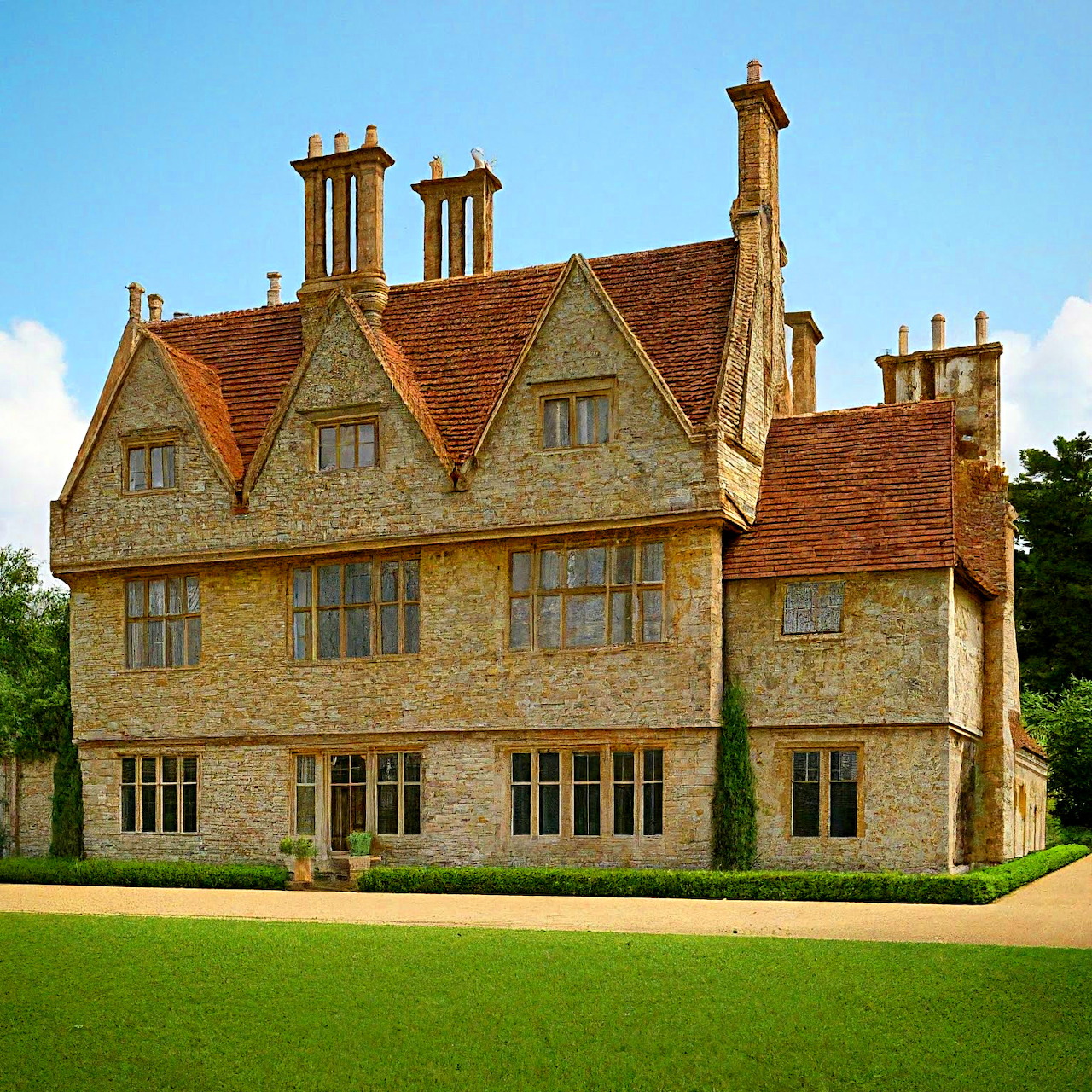 Stone English manor house with decorative chimneys and orange tiled roof on green lawn