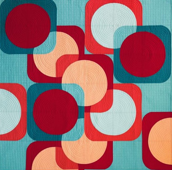 Geometric quilt with red, teal, and peach circles and rounded squares on turquoise fabric