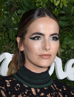 Close-up of a woman with dramatic cat-eye makeup, dark hair pulled back, wearing a black lace top