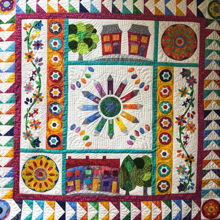 Colorful patchwork quilt with geometric shapes, flowers, houses, and circular mandala patterns in bright fabric squares