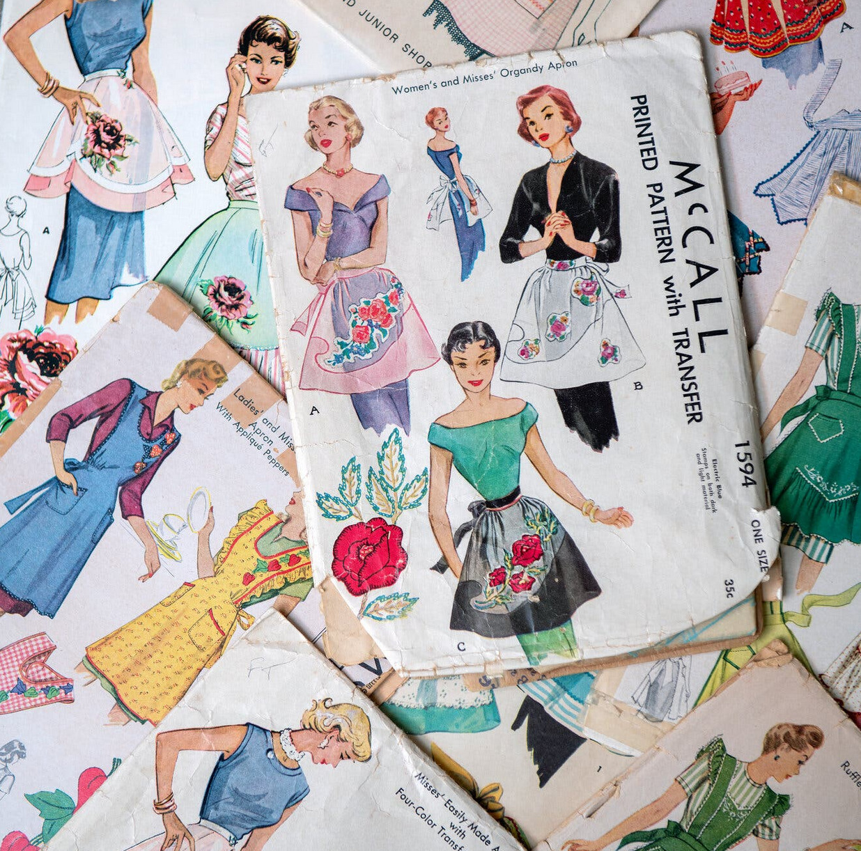 Overlapping vintage sewing pattern sheets with illustrated women wearing colorful aprons