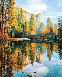 Stone bridge and autumn trees reflected in calm water below tall granite cliffs