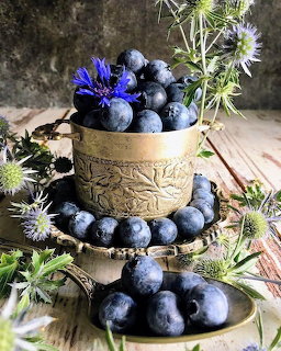 Blueberries in an ornate bowl with purple flowers on a rustic wooden table