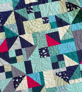 Geometric patchwork quilt with triangles and squares in teal, navy, cream, pink and gray with quilted stitching