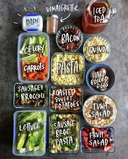 Overhead shot of labeled meal prep containers with pasta, vegetables, eggs, bacon, and salads on a dark table