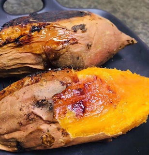 Two baked sweet potatoes on a dark plate, one split open showing orange flesh with butter