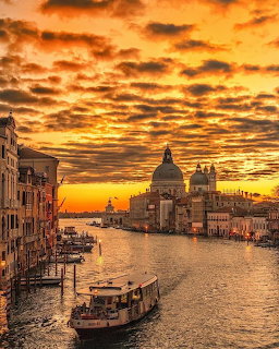 Dramatic golden sunset over the Grand Canal in Venice with domed basilica and boats