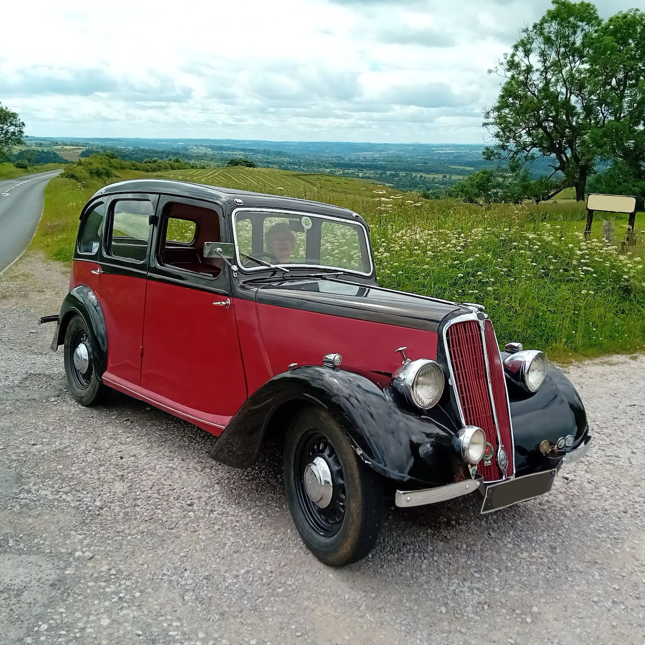 Red and black 1938 Jowett 8hp vintage car on hillside road with countryside view