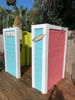 Two colorful wooden outdoor shower stalls on a deck with palm trees in the background