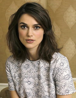 Portrait of Keira Knightley wearing a light patterned top against beige wallpaper