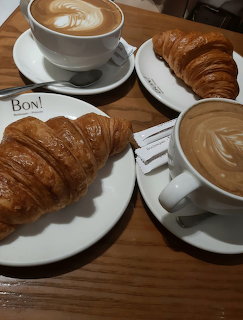 Two croissants on plates with two cups of latte art coffee on a wooden table