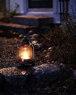 Lit lantern on a stone path at dusk near a house entrance
