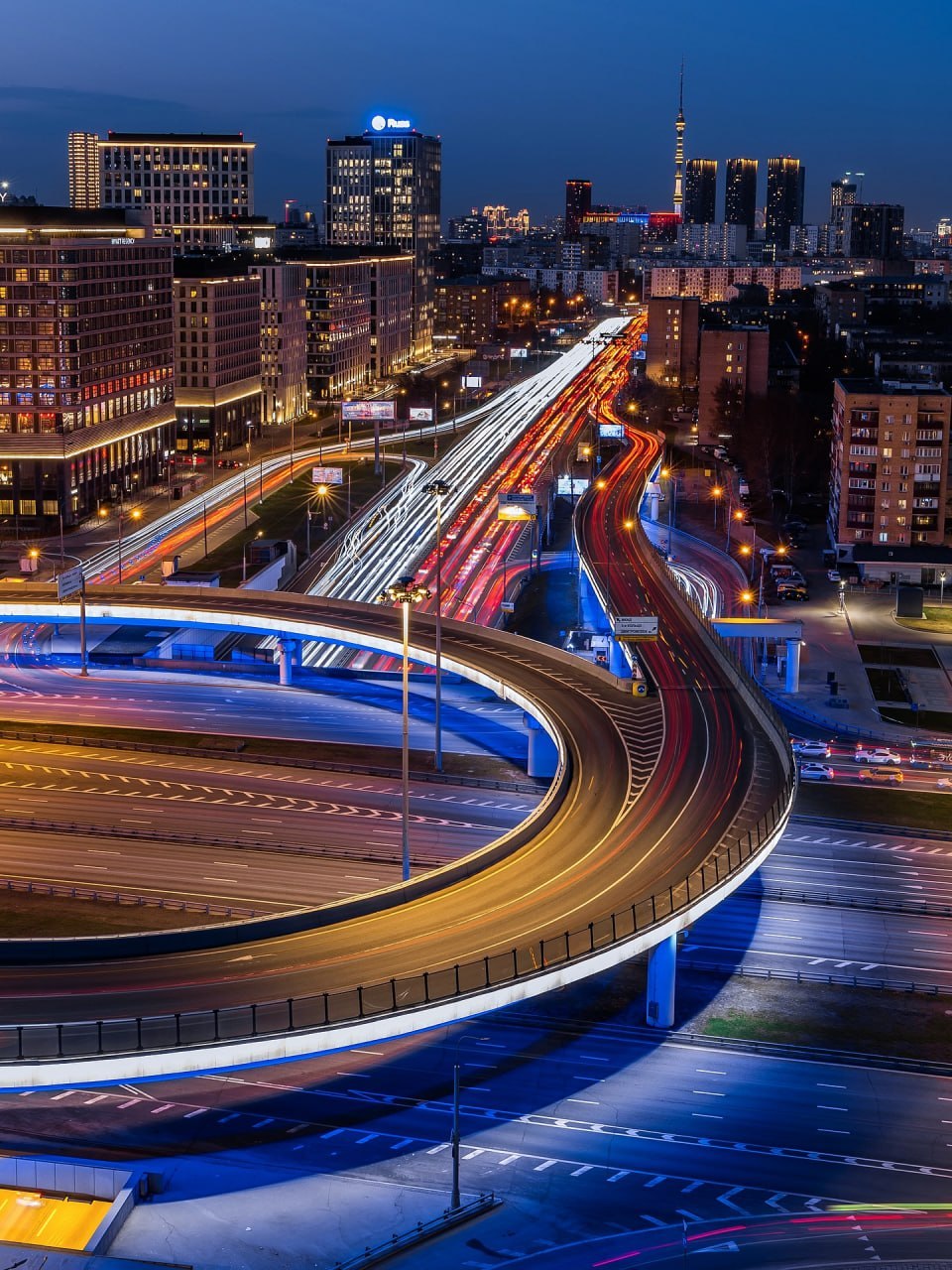 Aerial view of Moscow highways with light trails at dusk, curved roads and city buildings illuminated