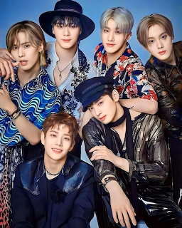 Six stylish young men posing together in colorful patterned outfits against a blue background