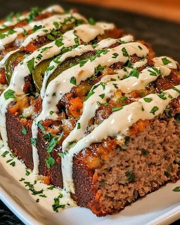 Sliced meatloaf with cheese filling, jalapeños, and ranch drizzle garnished with herbs