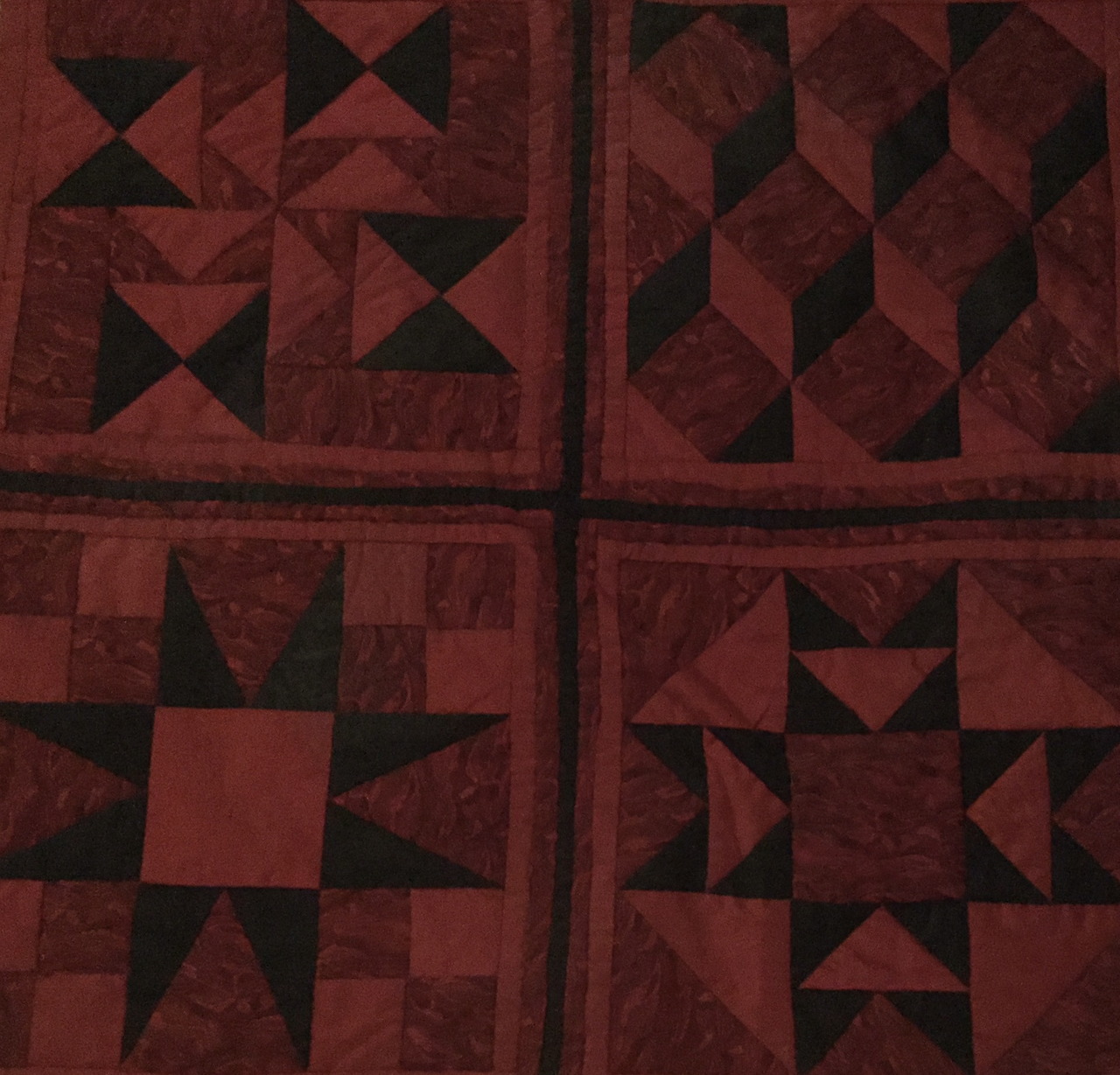 Red patchwork quilt with geometric star patterns in four blocks