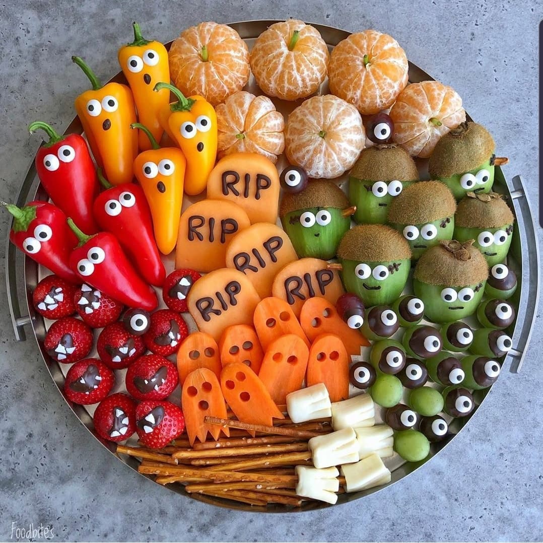 Halloween vegetable platter with peppers, pumpkins, and veggies decorated with candy eyes and arranged in festive characters