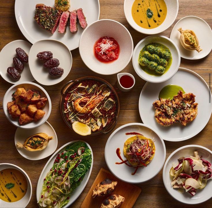 Overhead view of multiple gourmet dishes on white plates arranged on wooden table