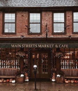 Brick exterior of Main Streets Market & Cafe with autumn pumpkin displays and string lights on a rainy day