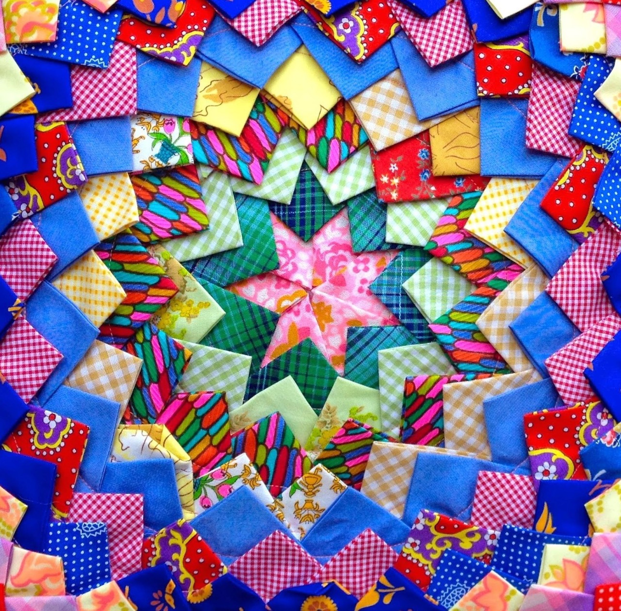 Colorful quilted star pattern with geometric fabric pieces in pink, green, yellow, and red on checkered blue border