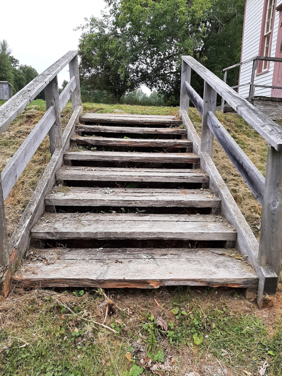 Weathered wooden stairs with railings on a grassy slope outdoors