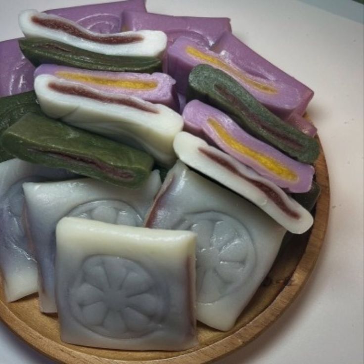 Close-up of assorted purple, green, and white rice cakes with red bean filling in a wooden bowl