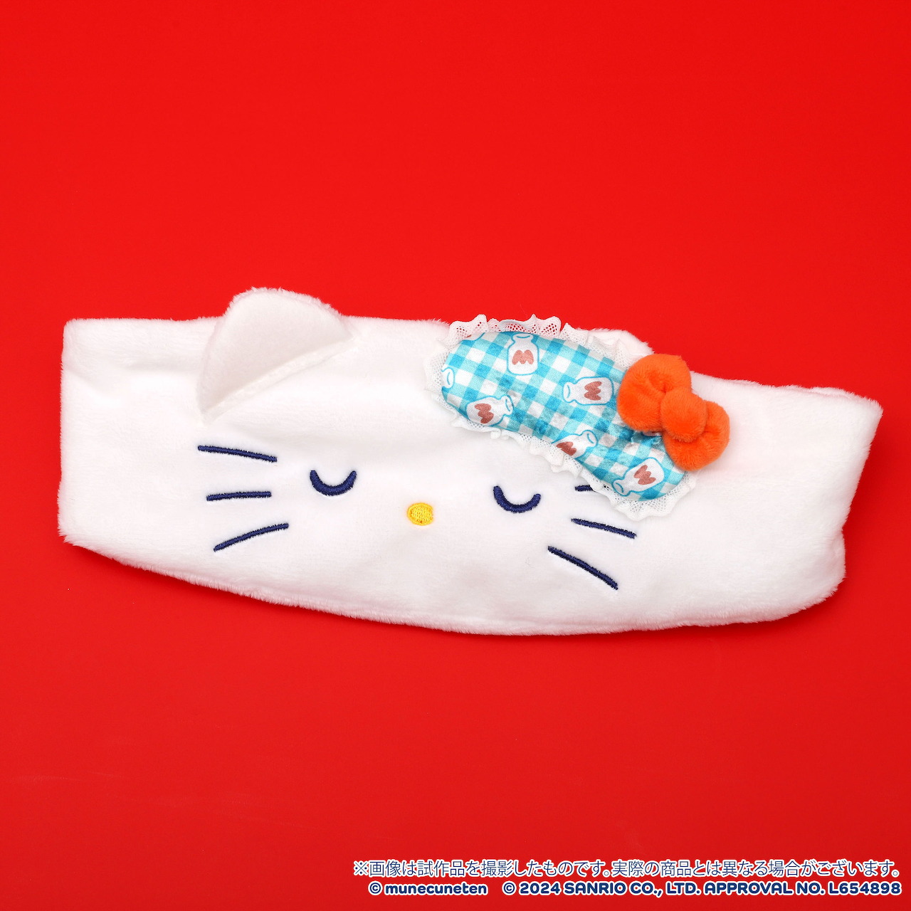 White plush Hello Kitty hairband with blue gingham lining and orange bow on red background