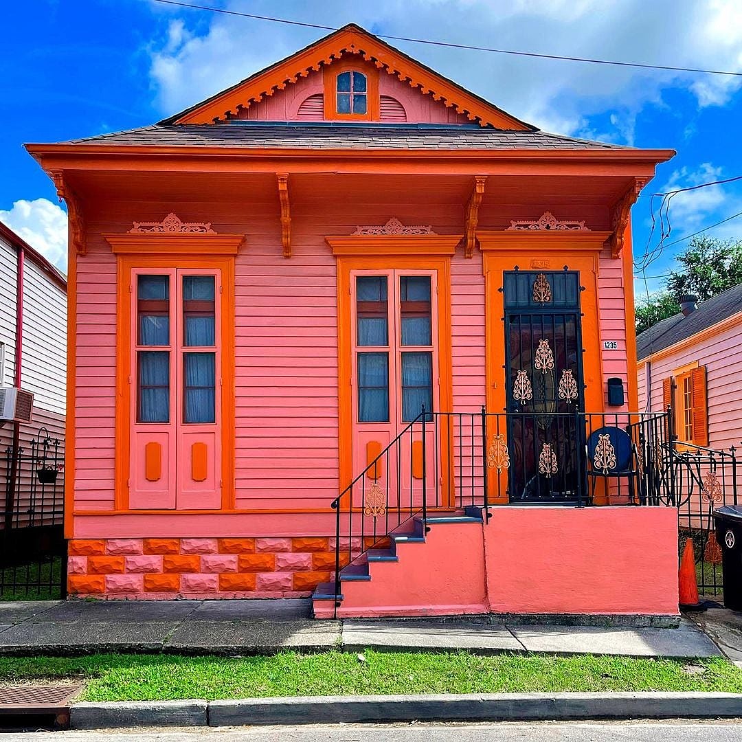 Bright pink and orange house with blue trim, front steps, and a black door