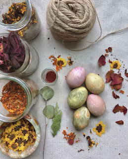 Naturally dyed eggs in pastel colors with jars of dried flowers, leaves, and twine on linen fabric
