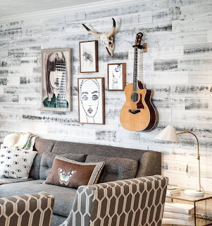 Living room with gray sofa, acoustic guitar on white wood wall, framed art, and animal skull decor