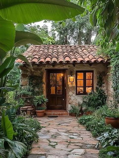 Small stone cottage with red tile roof surrounded by dense tropical foliage and garden pathway