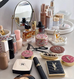 Flatlay of luxury makeup and beauty products including Chanel, YSL, and Dior items with a gold mirror