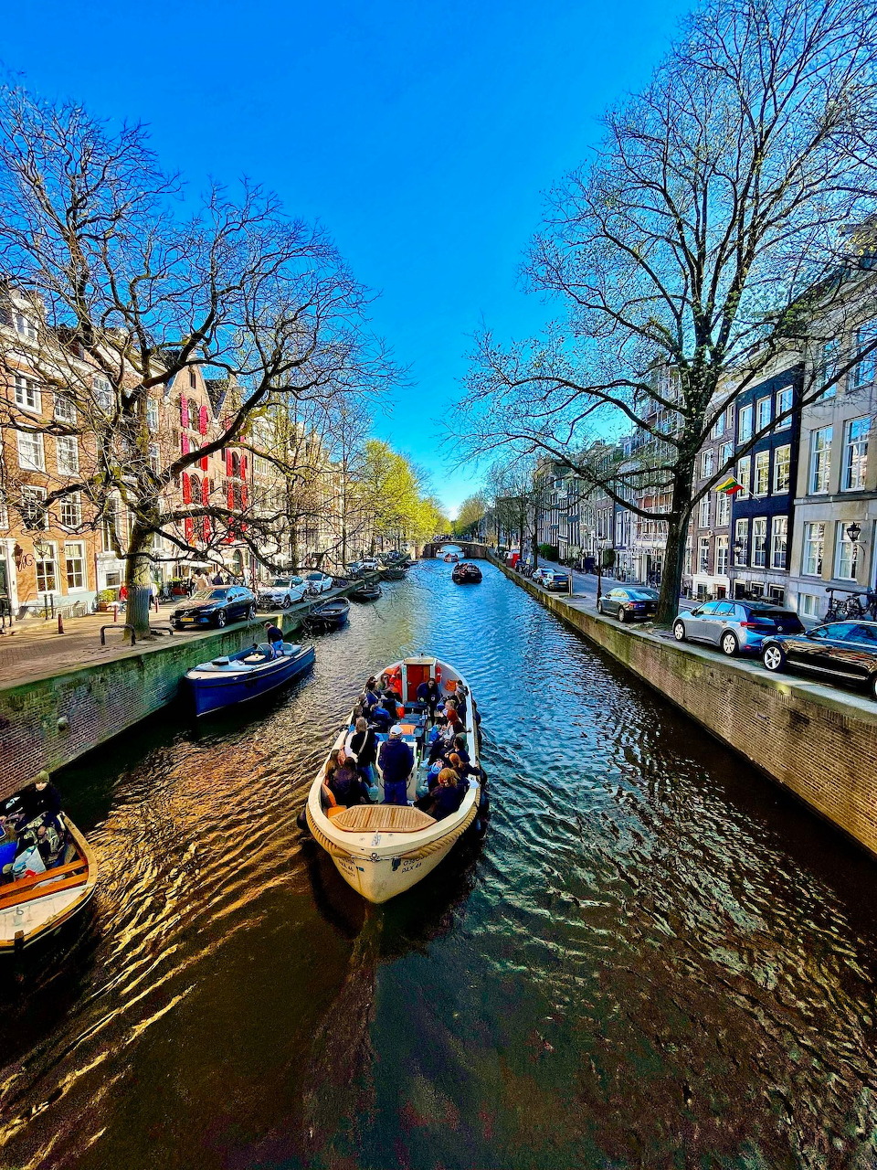 Canal in Amsterdam with boats traveling on water, flanked by bare trees and classic Dutch architecture