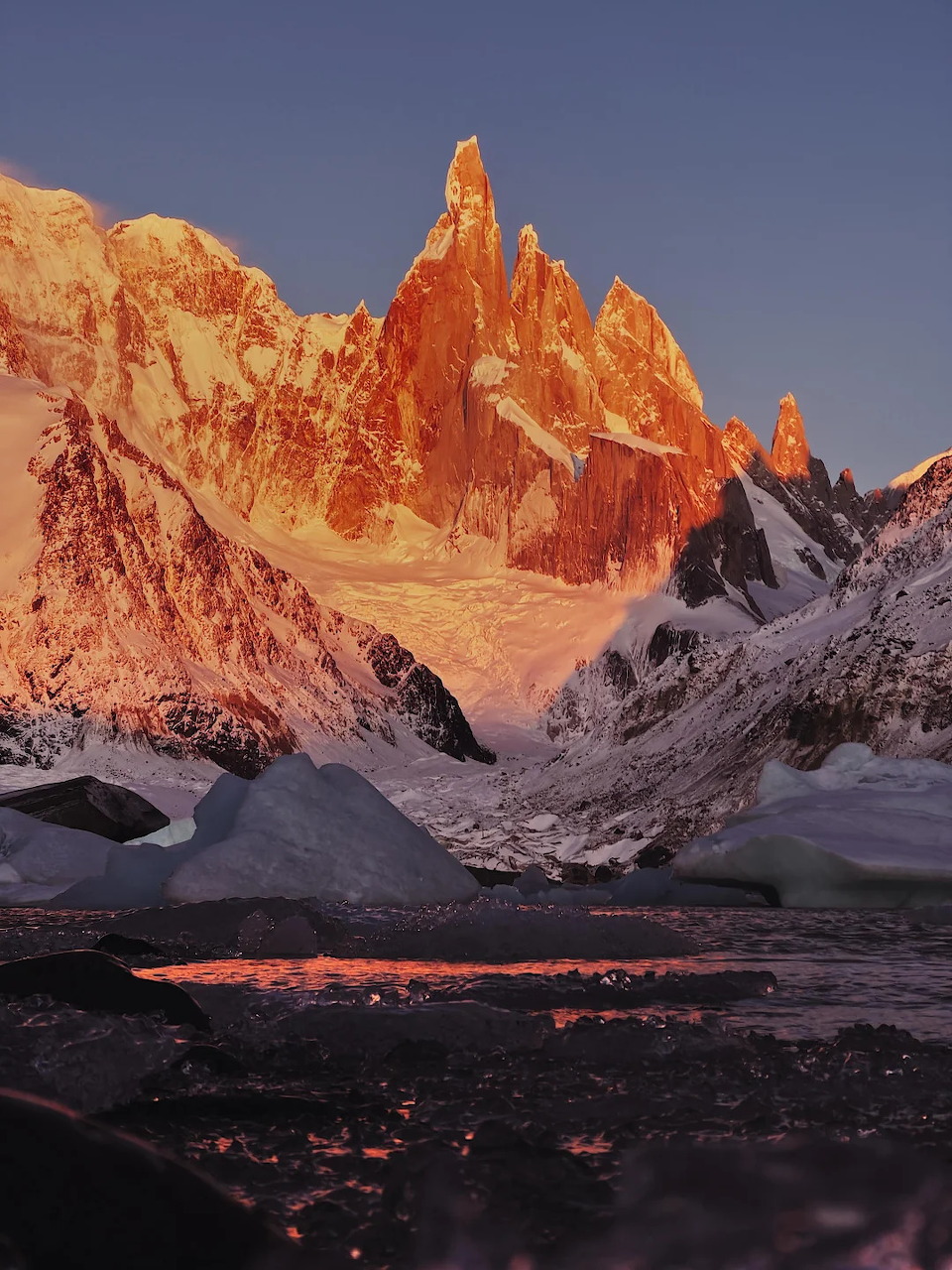 Cerro Torre mountain peak glowing orange at sunset above snowy glacial valley in Patagonia